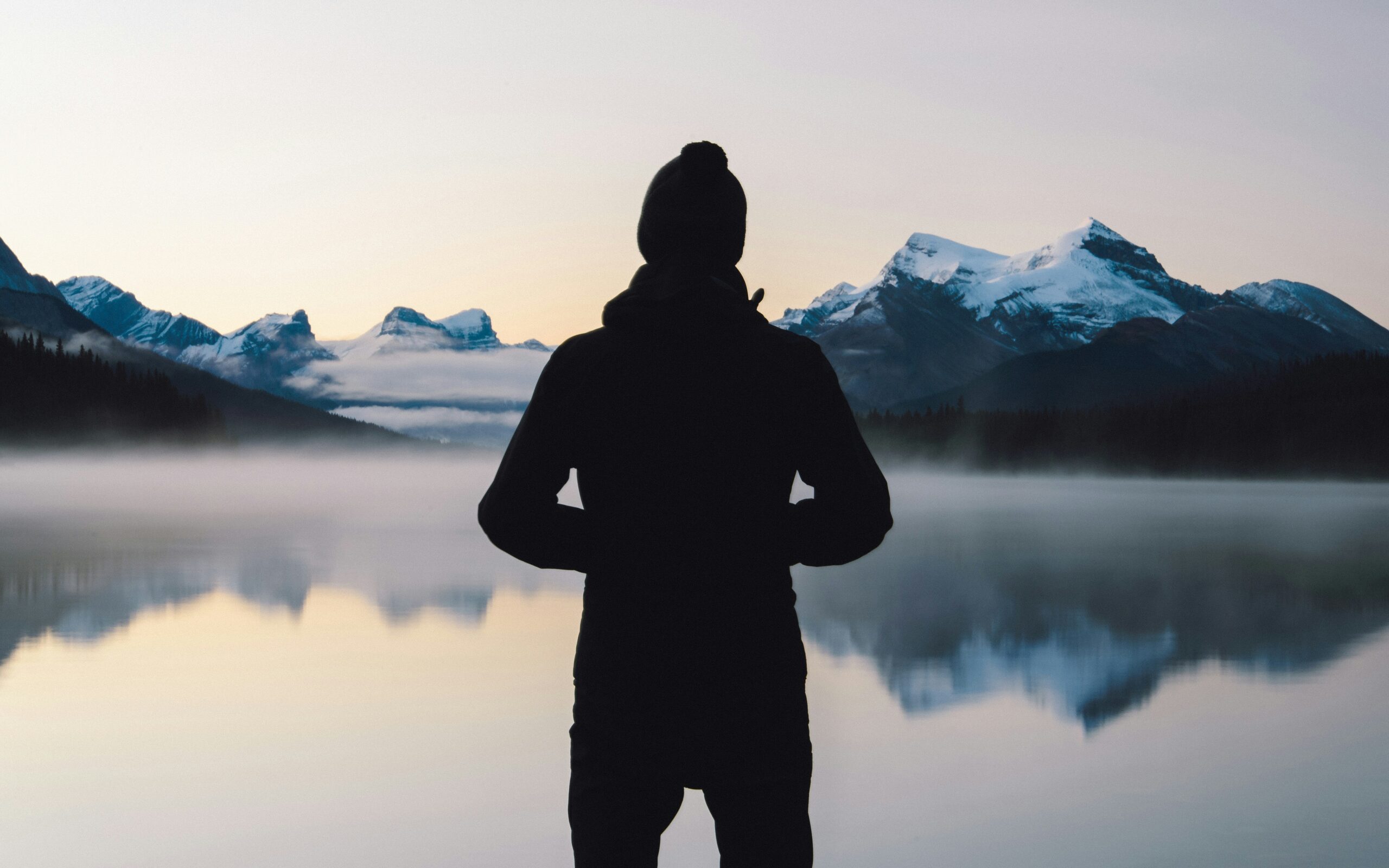 A solitary figure in reflection, observing a tranquil and perfectly clear alpine lake at sunrise, illustrating the mental clarity and stillness of mindfulness practice."